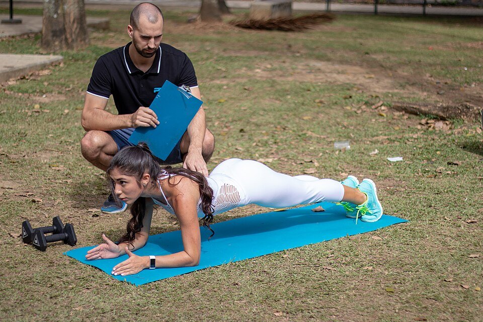 Person holding a high plank position outdoors while a trainer observes form